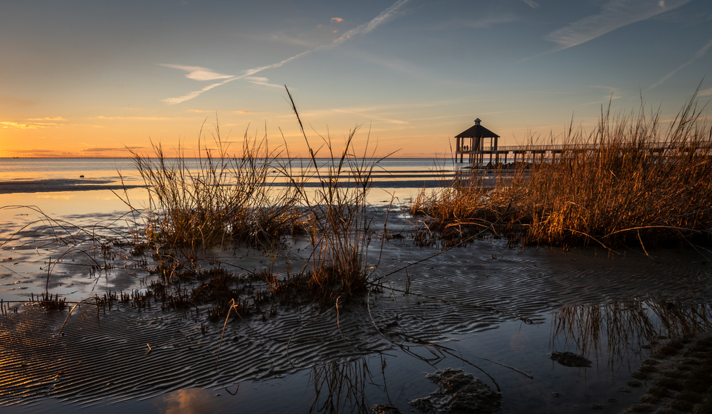 Lake during sunset with a pier in the background and grass in the foreground