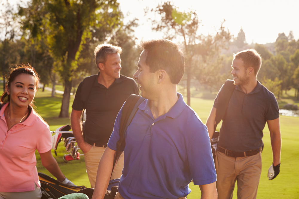 four people walking on a golf course with their golf clubs