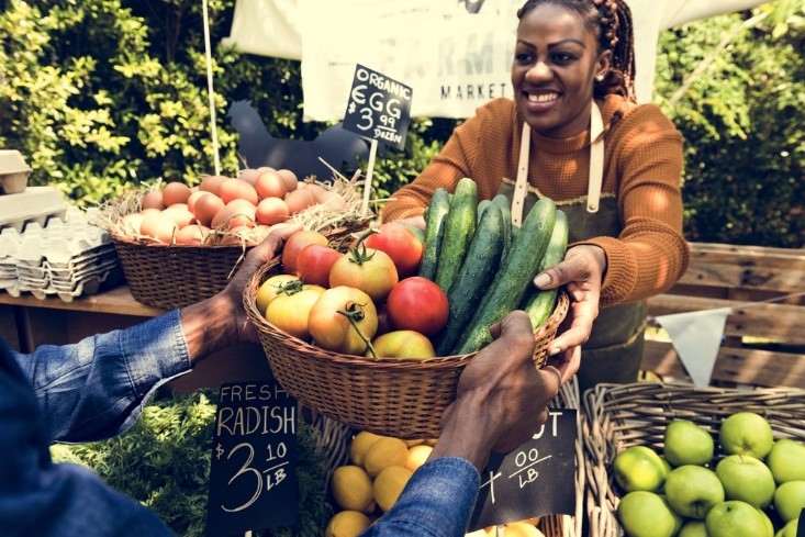 african american woman at farmers market holding fruits and vegetables